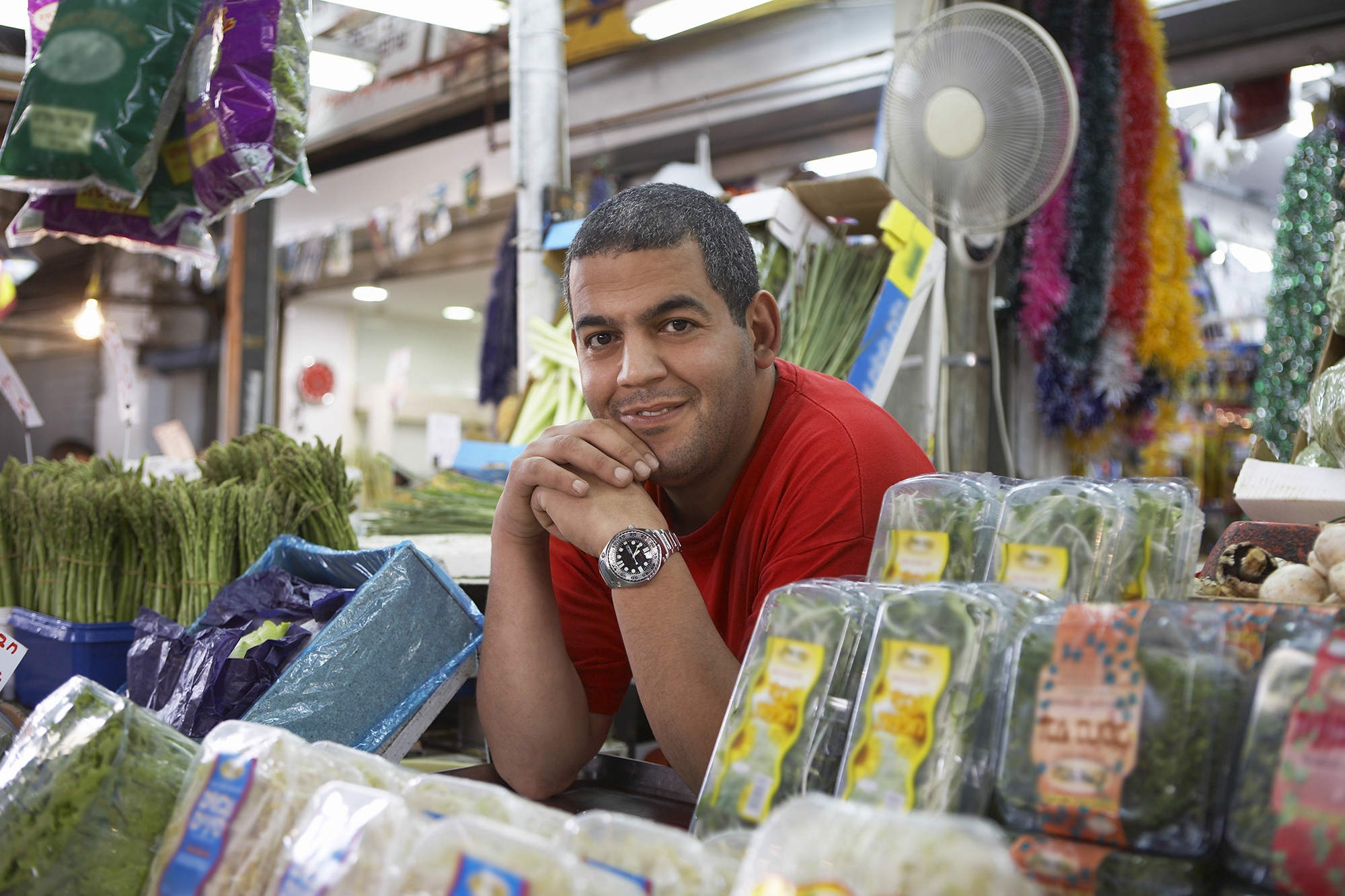 Retrato de un hombre sonriendo y apoyado en una mesa de un mercado de agricultores.