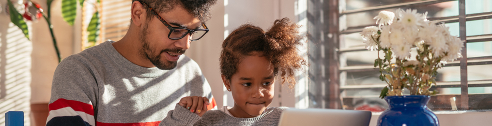 Father and child working on a laptop at a kitchen table