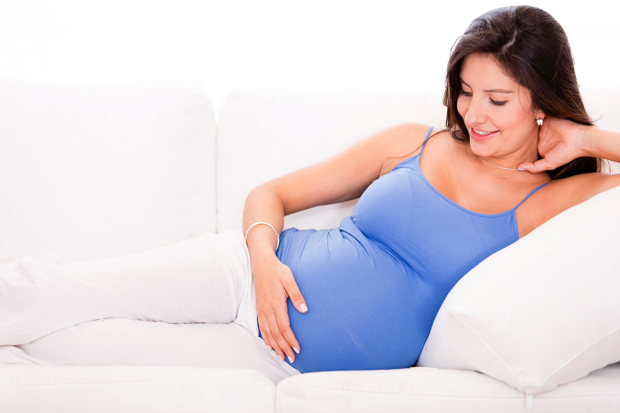 A pregnant woman smiles at her baby bump