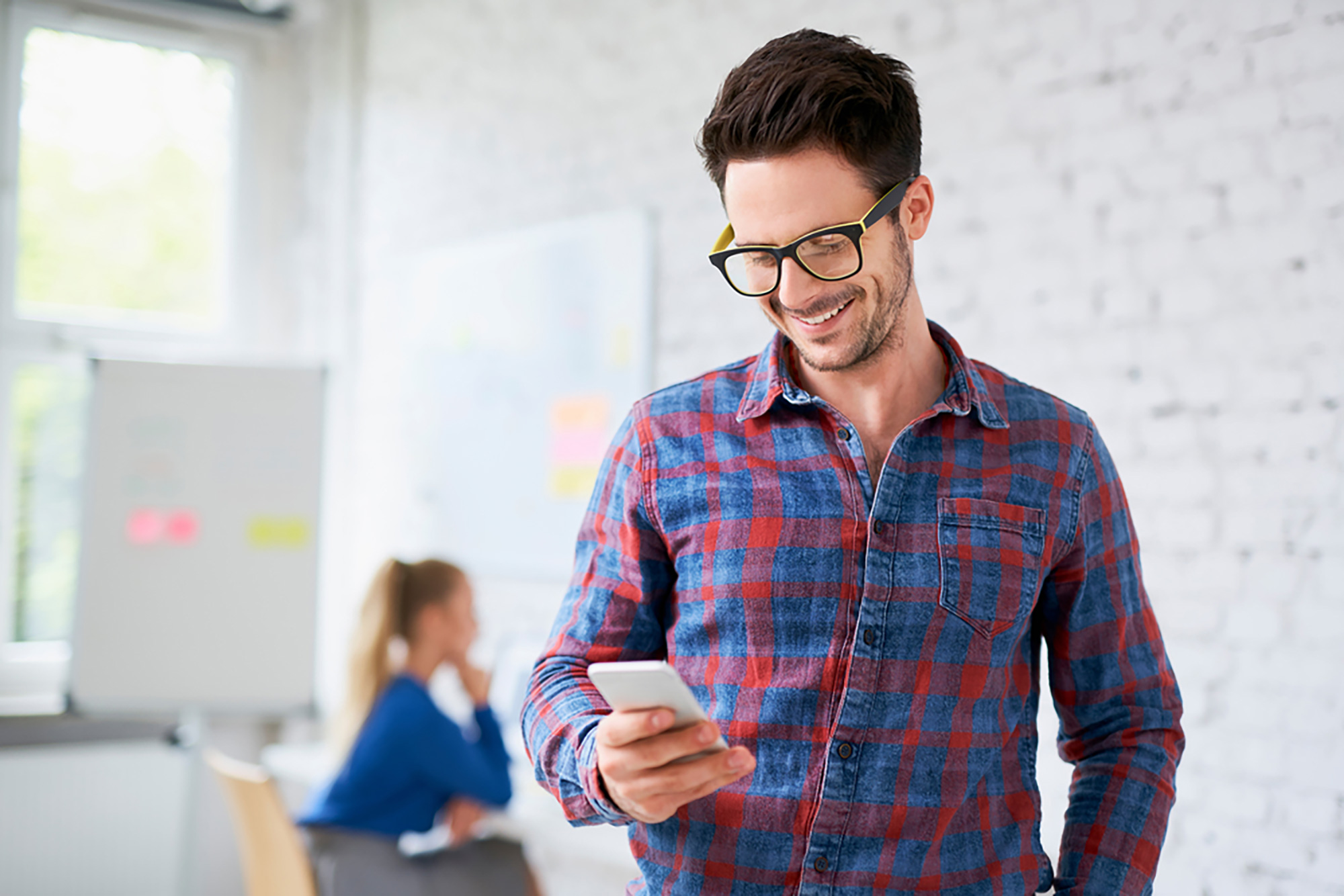 Un hombre con una camisa de cuadros azul mira a su teléfono inteligente y sonríe