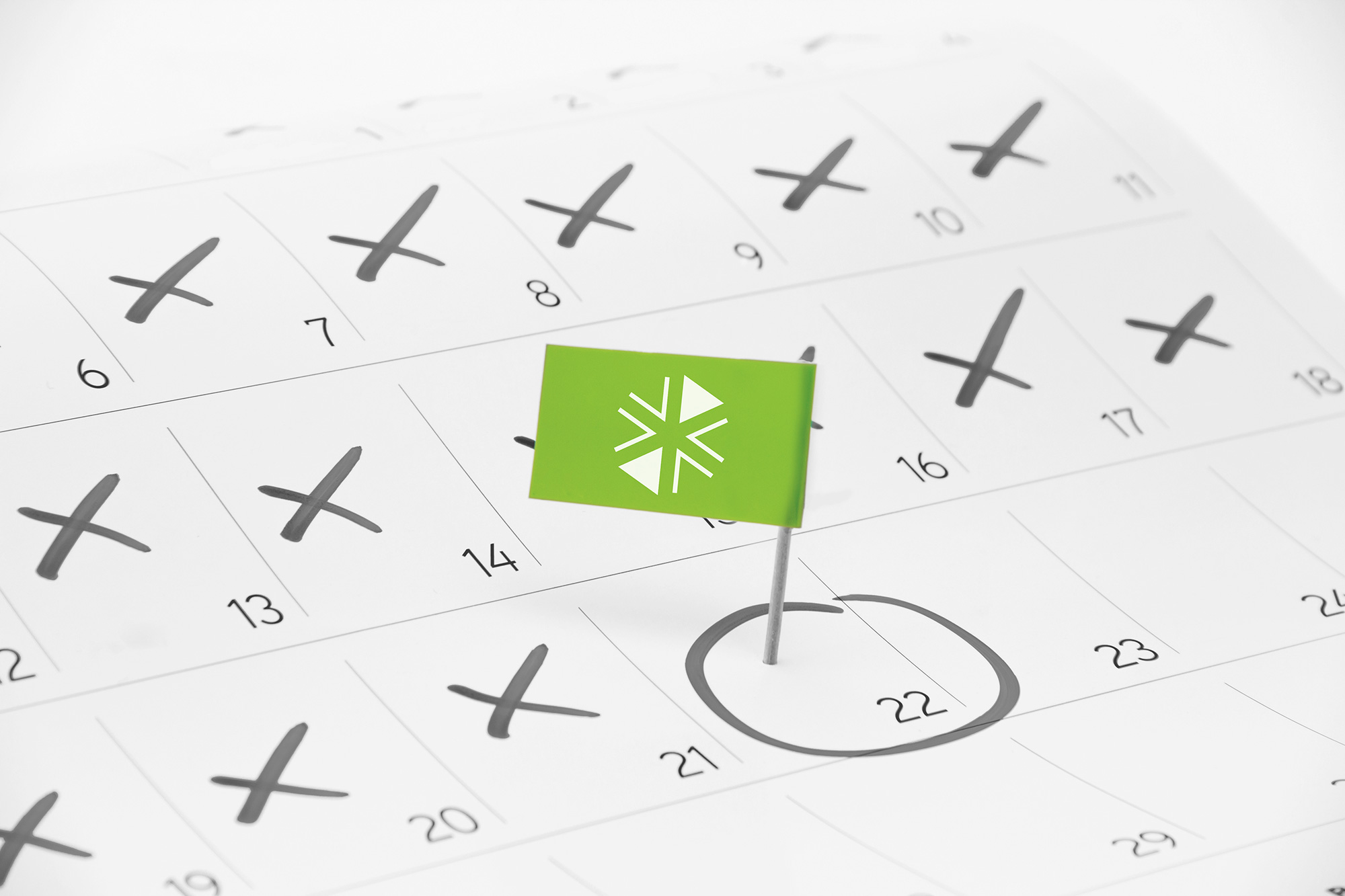 Acercamiento de un calendario con un día encerrado y marcado con una bandera verde clavada con un alfiler.