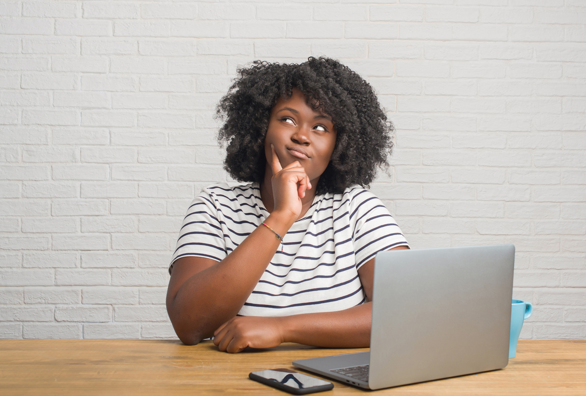 Una mujer hace un gesto de duda mientras está sentada frente a una computadora portátil abierta.