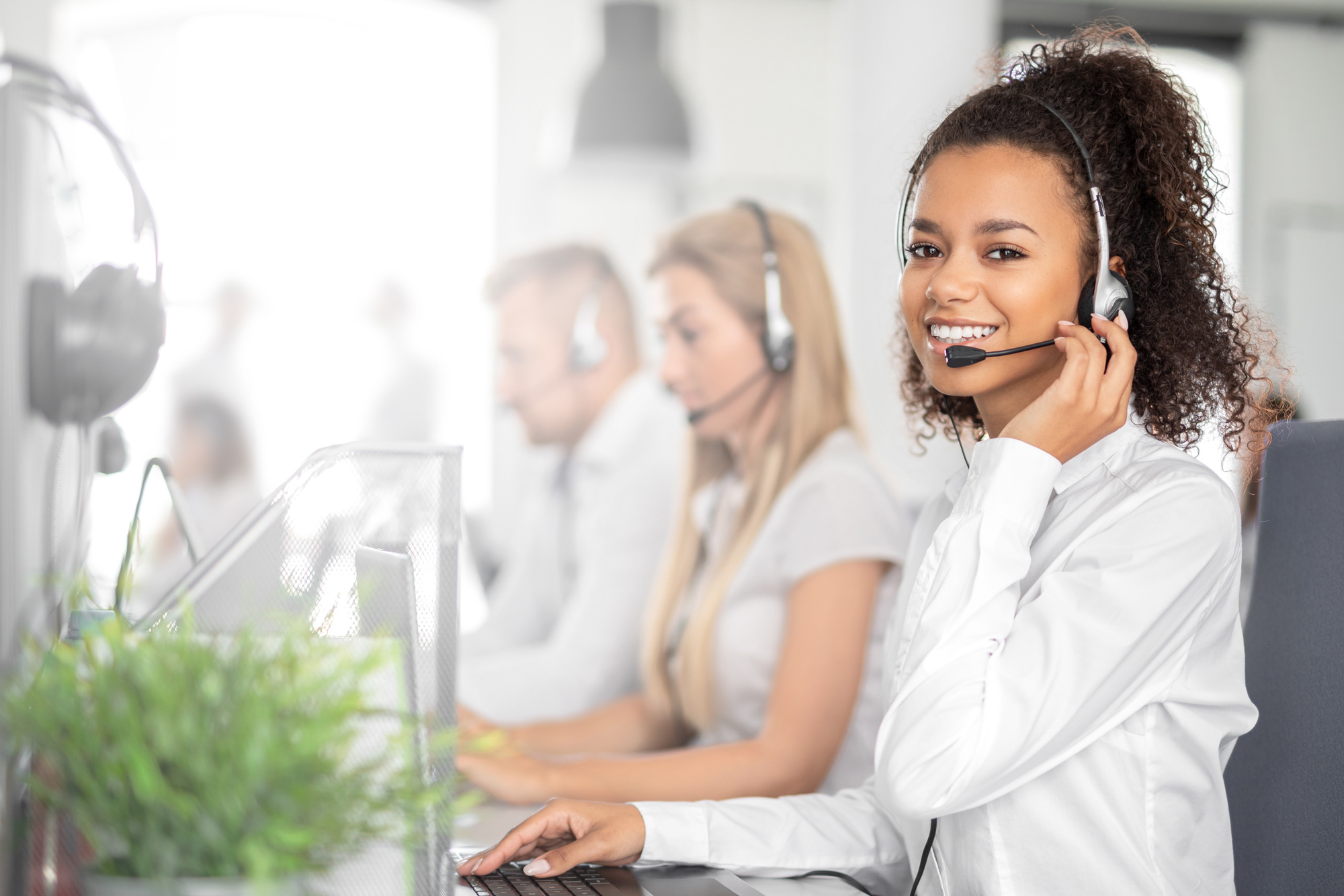 Una representante de servicio al cliente con auriculares sentada frente a un teclado. Está viendo a la cámara y sonriendo.